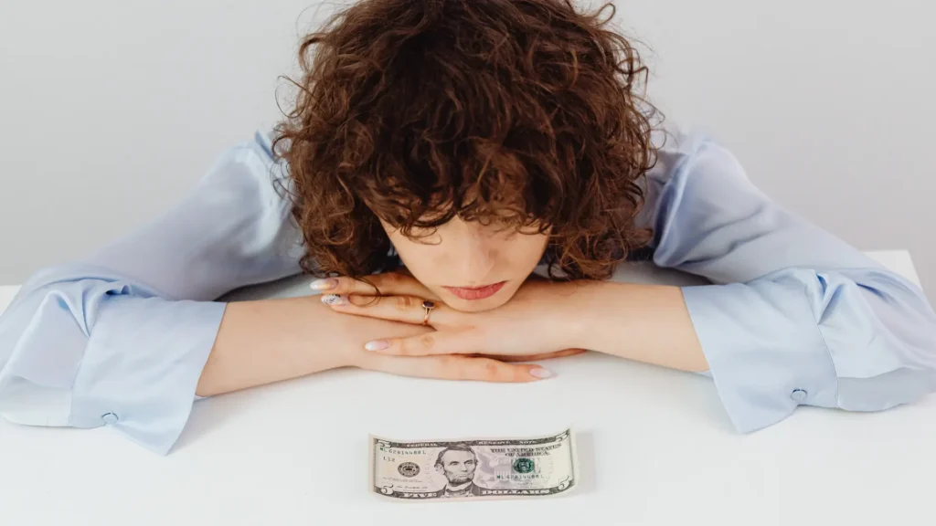 Mujer viendo tristemente un dólar pensando en deudas por falta de buenos hábitos financieros