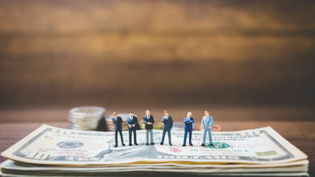 personas pequeñas parados en un dólar gigante representando los gastos hormiga.