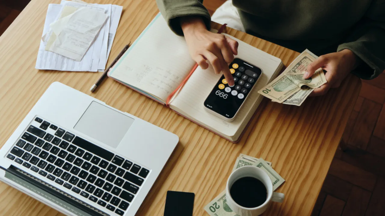 Persona administra sus finanzas con laptop, calculadora y dinero para separar las personales de las del negocio